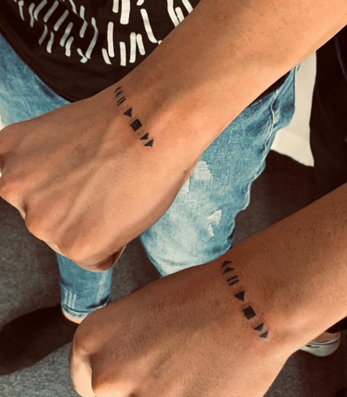 9 Minimalist Couple Tattoo Ideas Unique and Subtle for Lasting Ink 9 Two wrists displaying small black minimalist tattoos of media playback symbols.