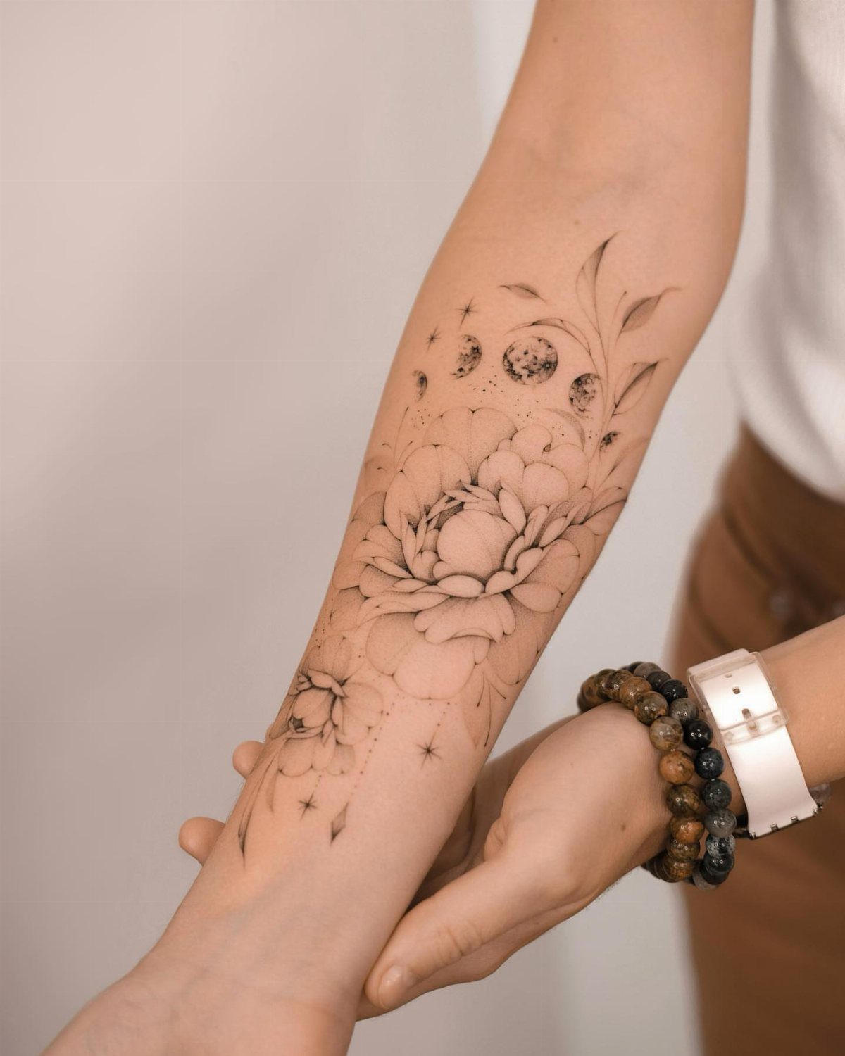 Moon Phases Tattoo Designs for Women: 8 Ideas to Consider 4 A forearm tattoo featuring a large peony flower combined with moon phases and botanical leaves.