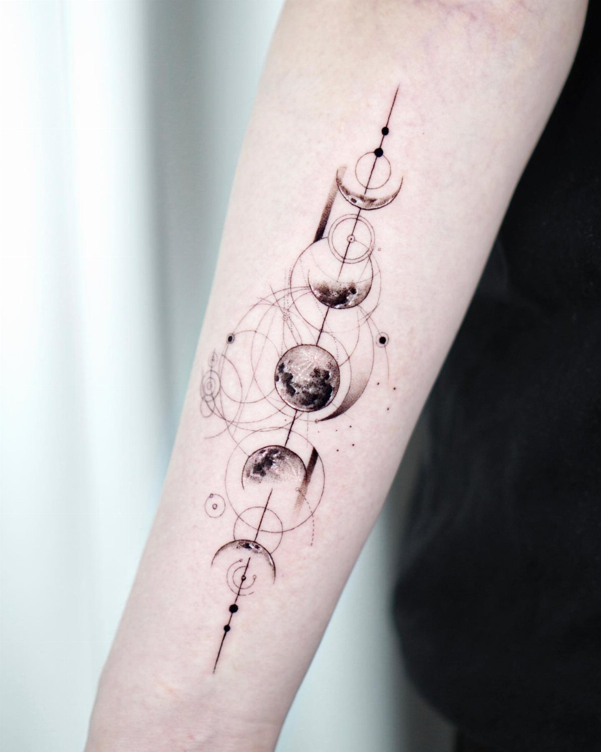 Moon Phases Tattoo Designs for Women: 8 Ideas to Consider 6 A vertical forearm tattoo depicting moon phases intertwined with delicate geometric circles and fine lines.