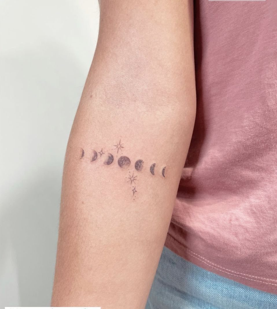 Moon Phases Tattoo Designs for Women: 8 Ideas to Consider 3 A horizontal moon phase tattoo with small stars on a person's forearm.