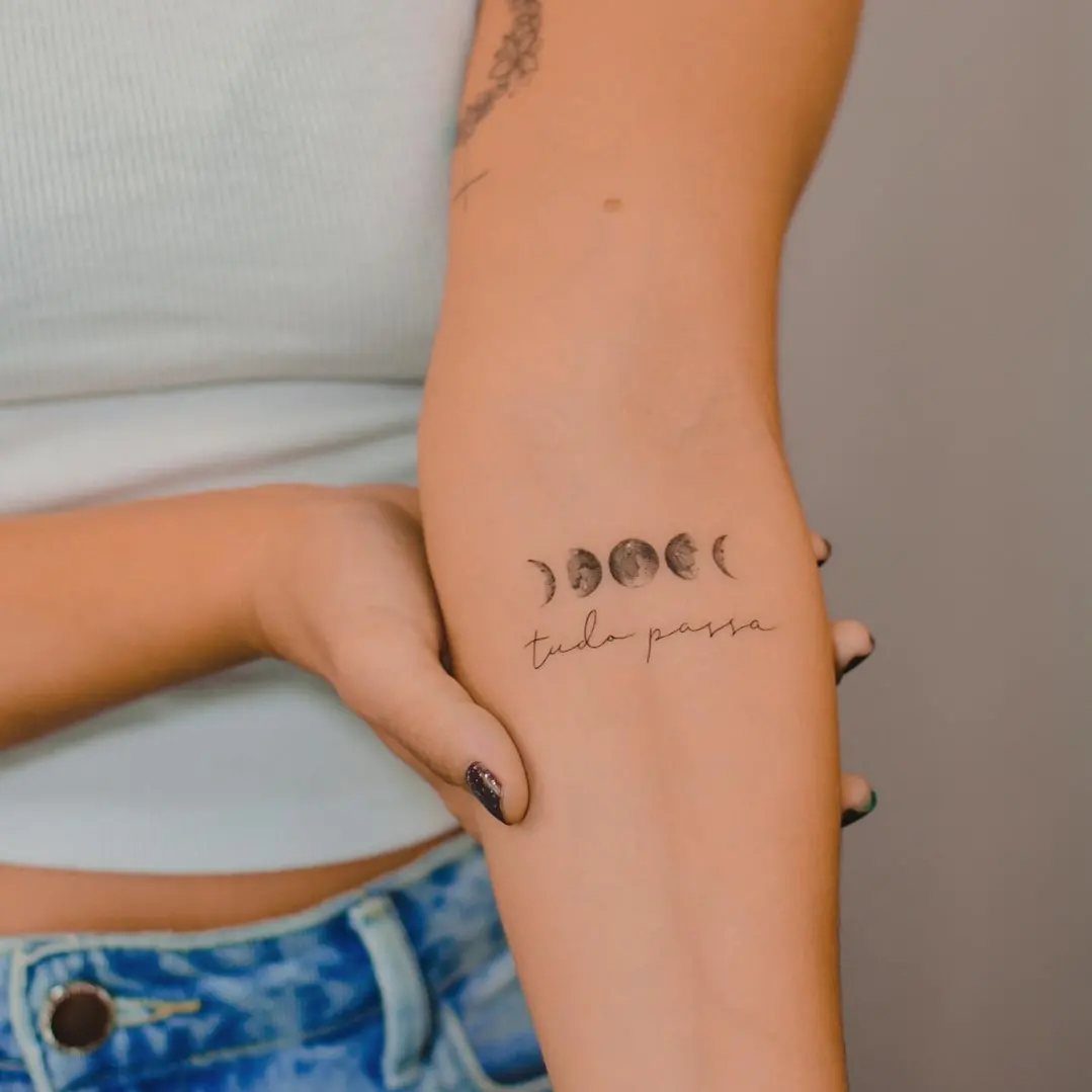 Moon Phases Tattoo Designs for Women: 8 Ideas to Consider 7 A person's arm displaying a moon phases tattoo with cursive text underneath.
