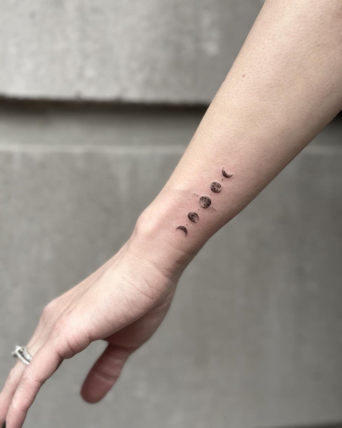 Moon Phases Tattoo Designs for Women: 8 Ideas to Consider 1 A vertical moon phase tattoo on a person's inner wrist against a neutral background.