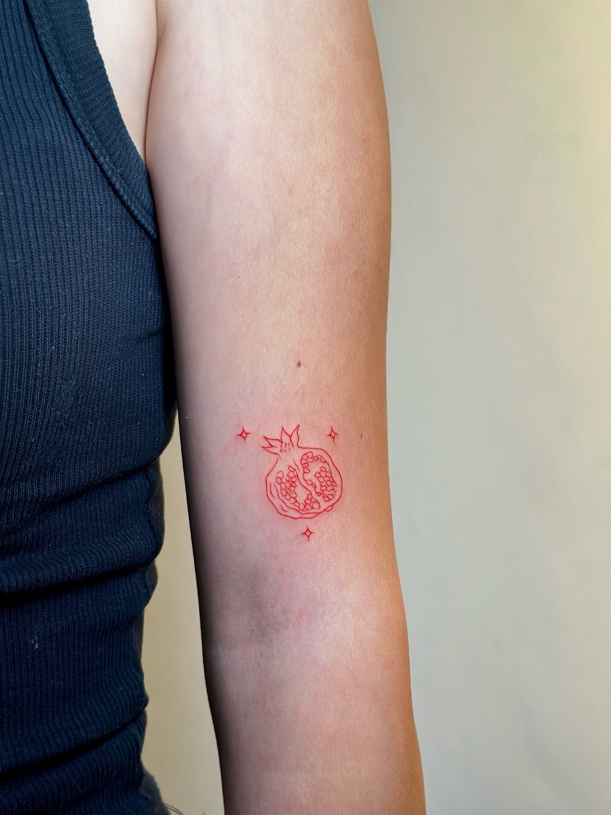 Pomegranate Tattoo Ideas: 11 Designs from Myth to Botanical 5 A small red fine line tattoo of a sliced pomegranate on a person's arm.