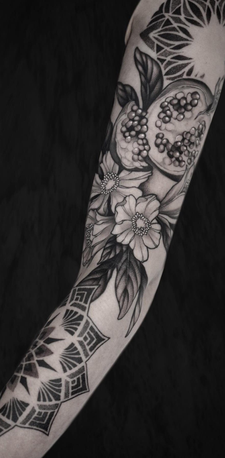 Pomegranate Tattoo Ideas: 11 Designs from Myth to Botanical 8 A black and grey arm tattoo featuring a sliced pomegranate and floral patterns.