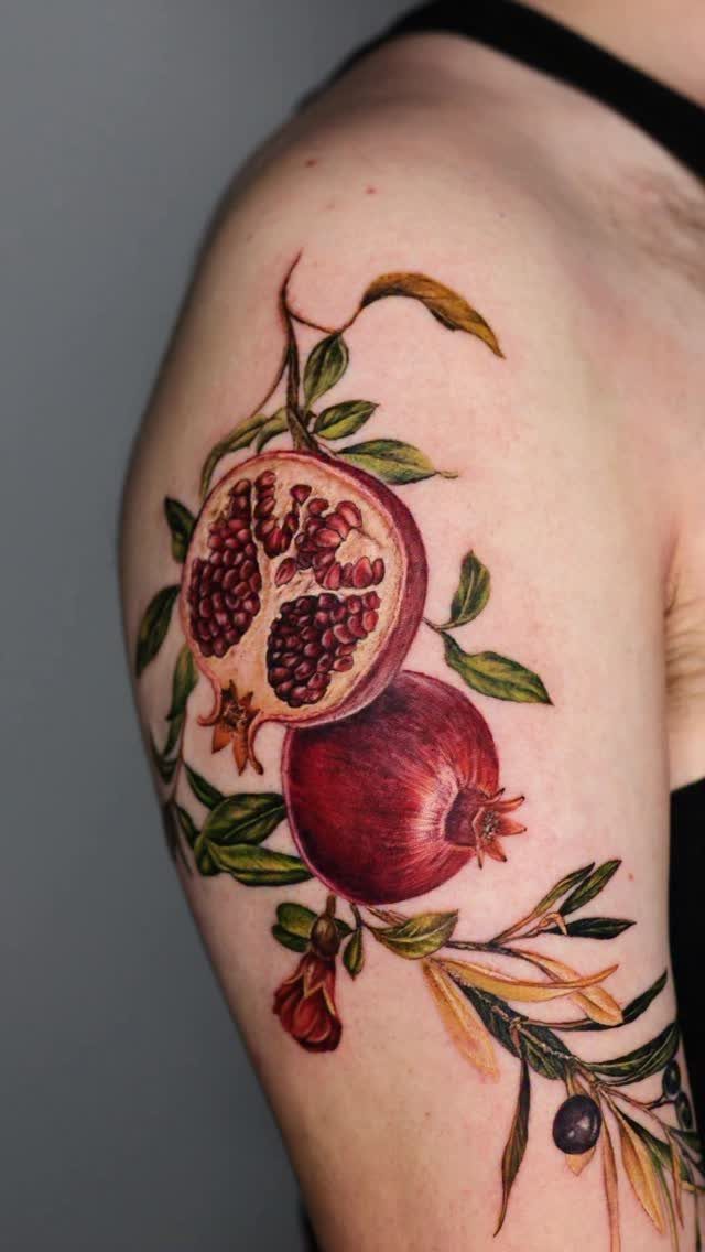 Pomegranate Tattoo Ideas: 11 Designs from Myth to Botanical 6 A colorful pomegranate tattoo with red seeds and green leaves on a person's shoulder.