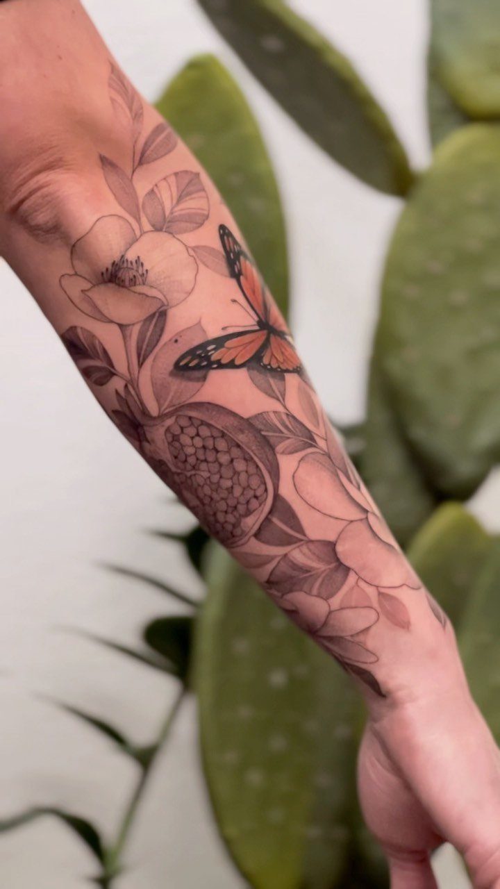 Pomegranate Tattoo Ideas: 11 Designs from Myth to Botanical 9 A forearm with a detailed tattoo of a pomegranate, flowers, and an orange butterfly.
