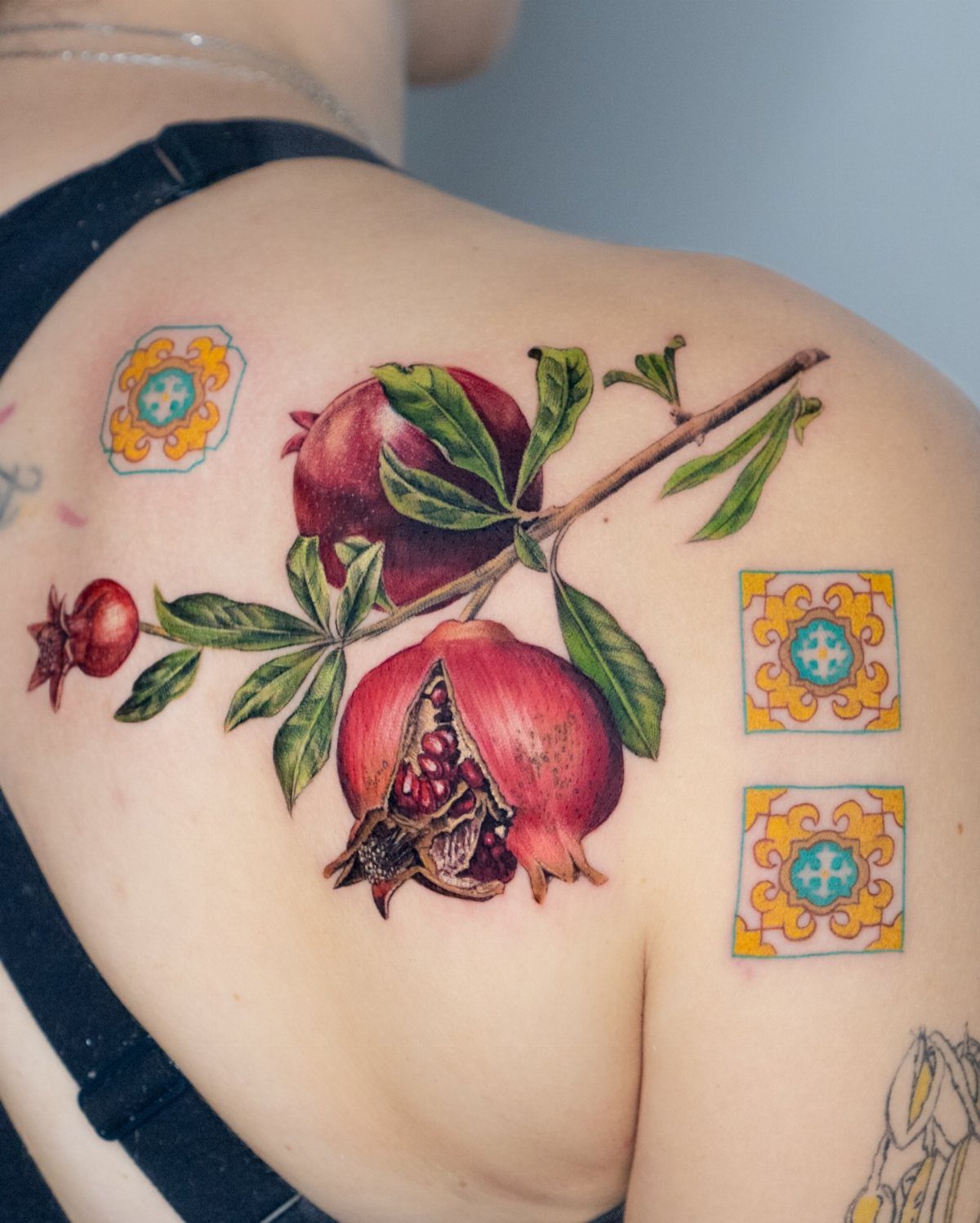 Pomegranate Tattoo Ideas: 11 Designs from Myth to Botanical 11 A detailed pomegranate tattoo with fruit and leaves on a person's shoulder.