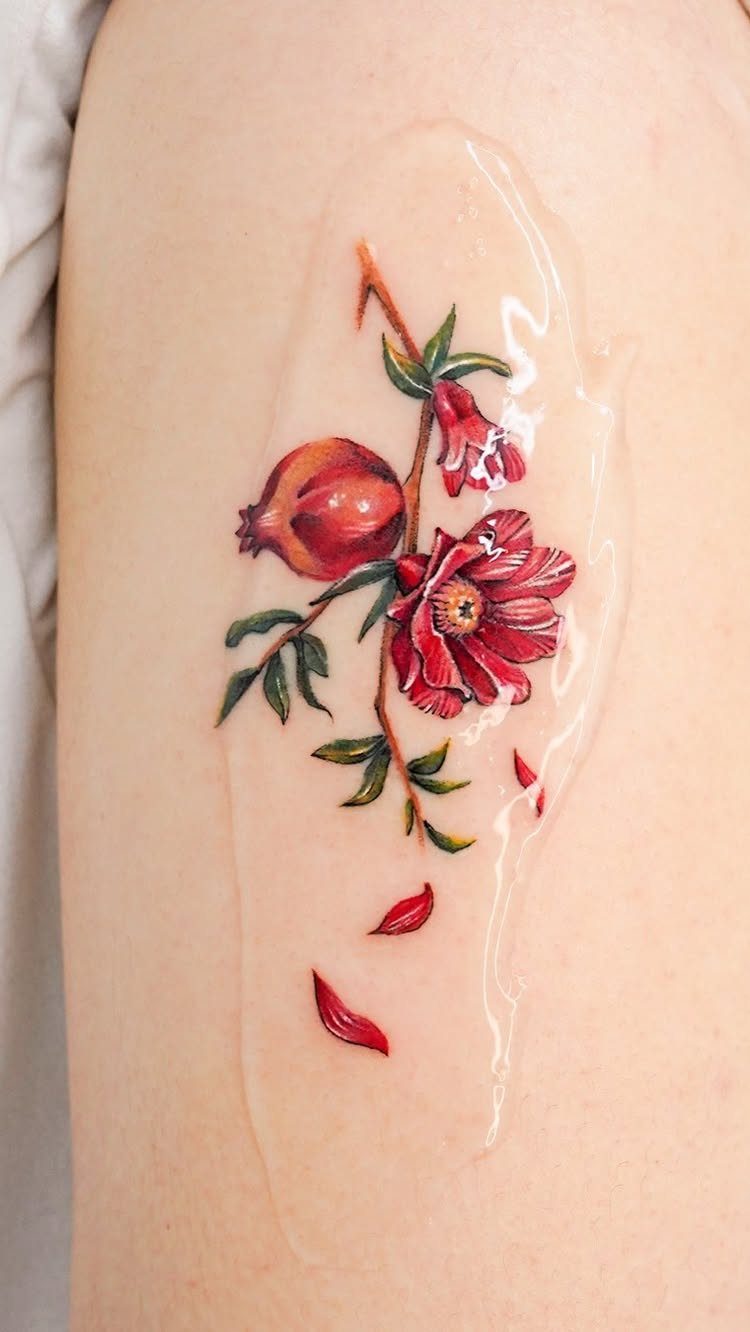 Pomegranate Tattoo Ideas: 11 Designs from Myth to Botanical 4 A vibrant pomegranate tattoo with red flowers and green leaves on human skin.