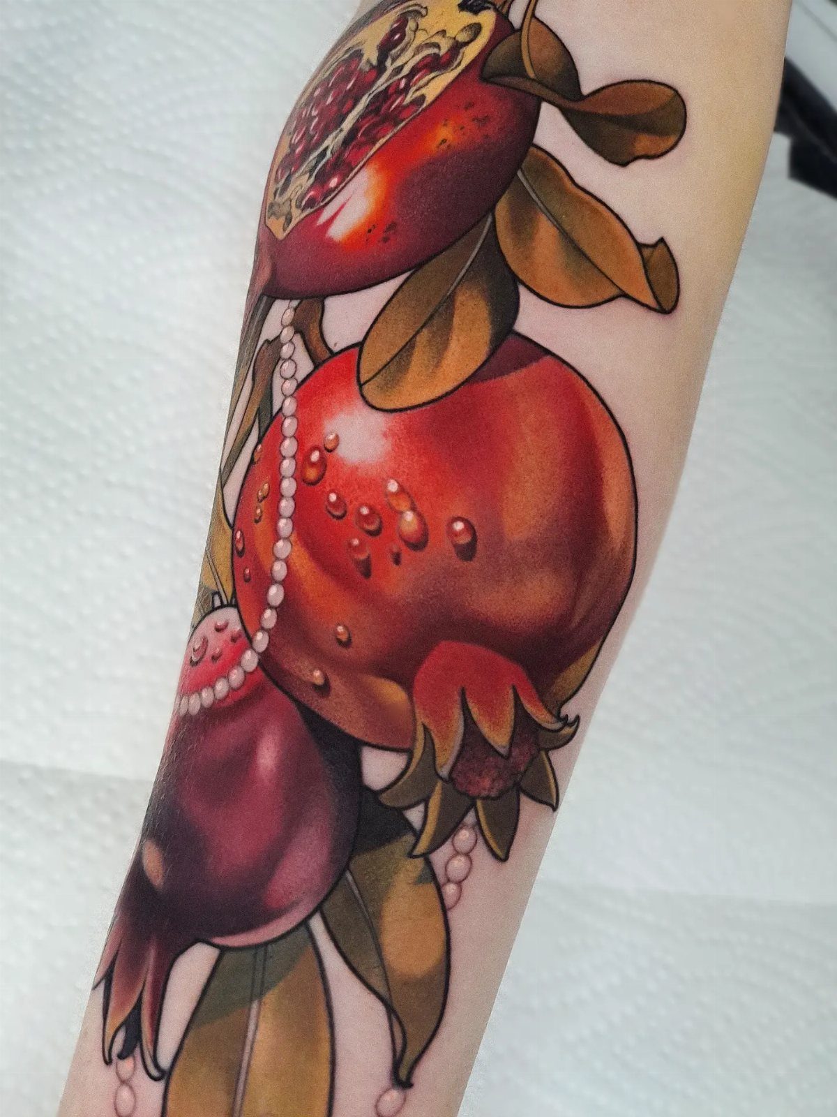 Pomegranate Tattoo Ideas: 11 Designs from Myth to Botanical 10 A vibrant pomegranate tattoo with red fruit, green leaves, and white pearls on a person's arm.