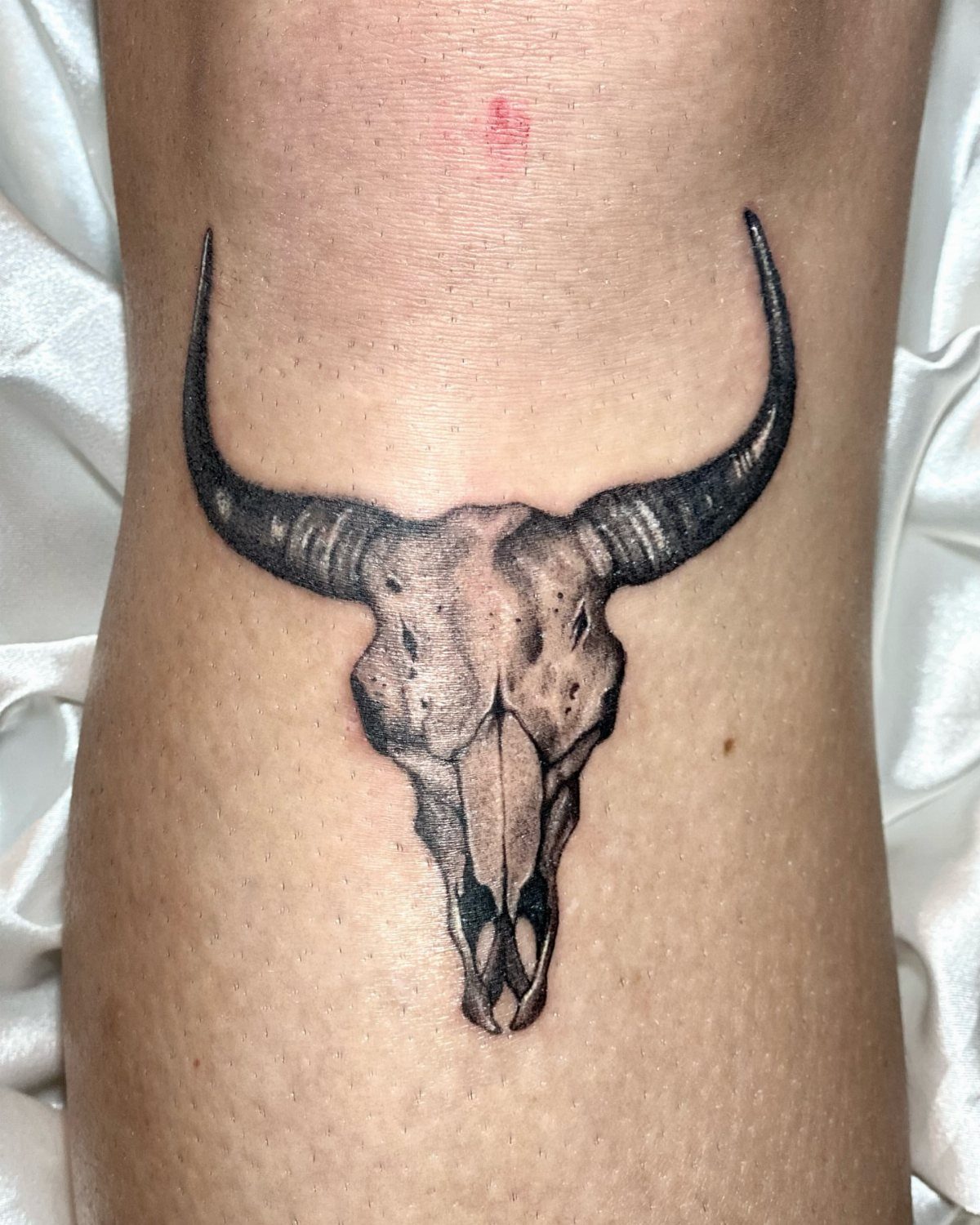 16 Realistic Bull Tattoo Ideas for Strength and Style 4 A realistic black and grey bull skull tattoo on human skin.