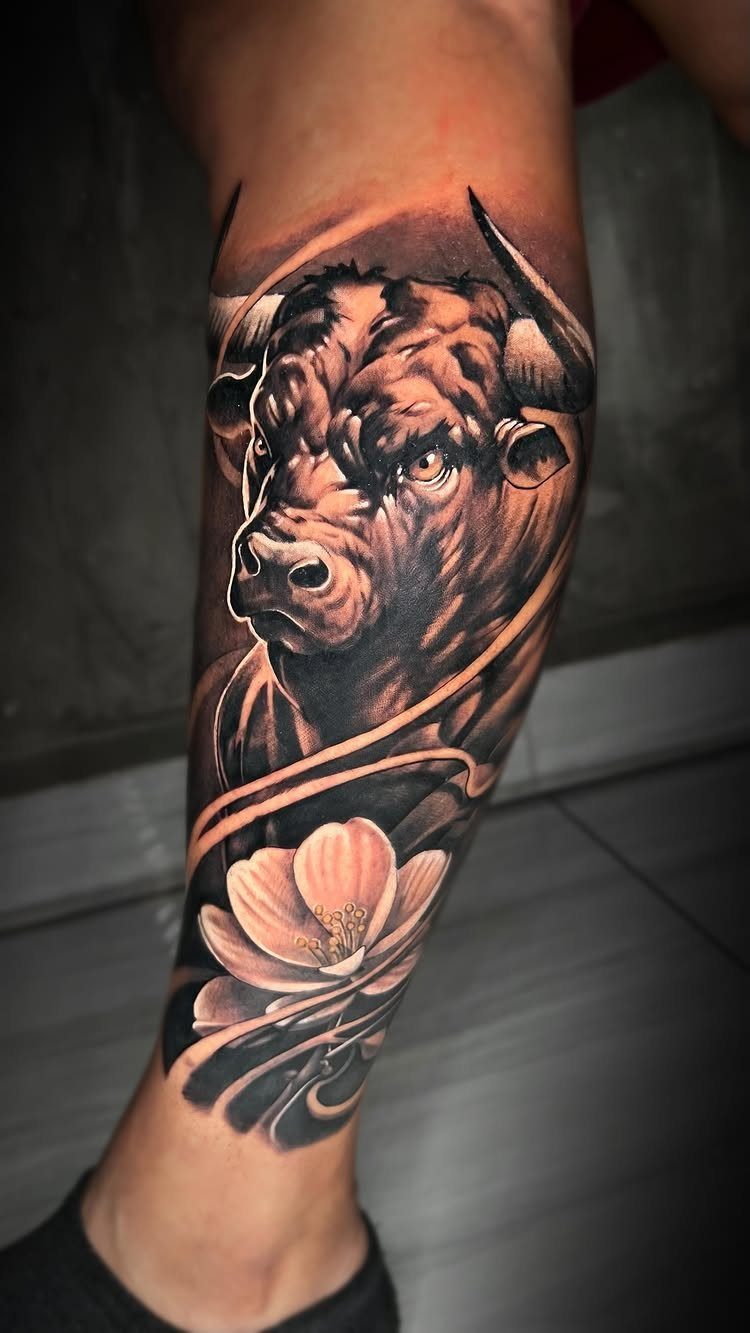 16 Realistic Bull Tattoo Ideas for Strength and Style 11 A detailed black and grey bull tattoo with a flower on a person's leg.