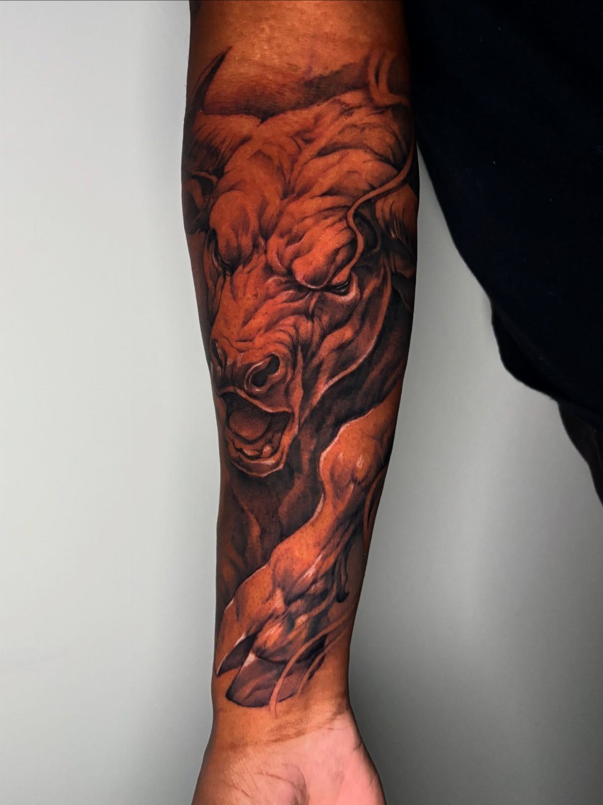 16 Realistic Bull Tattoo Ideas for Strength and Style 9 A detailed black and grey realistic bull tattoo covering a person's forearm.