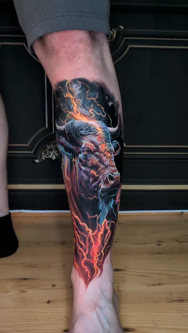 16 Realistic Bull Tattoo Ideas for Strength and Style 13 A detailed realistic bull tattoo with orange lightning effects on a person's lower leg.