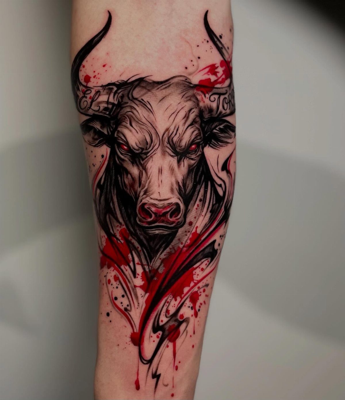 16 Realistic Bull Tattoo Ideas for Strength and Style 12 A detailed black and grey bull tattoo with red accents on a person's forearm.