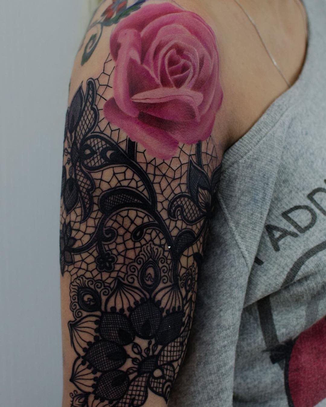 7 Rose with Pattern Tattoo Design Ideas for Ink That Stands Out 3 A large pink rose tattoo sits atop an intricate black lace pattern tattoo on a person's arm.
