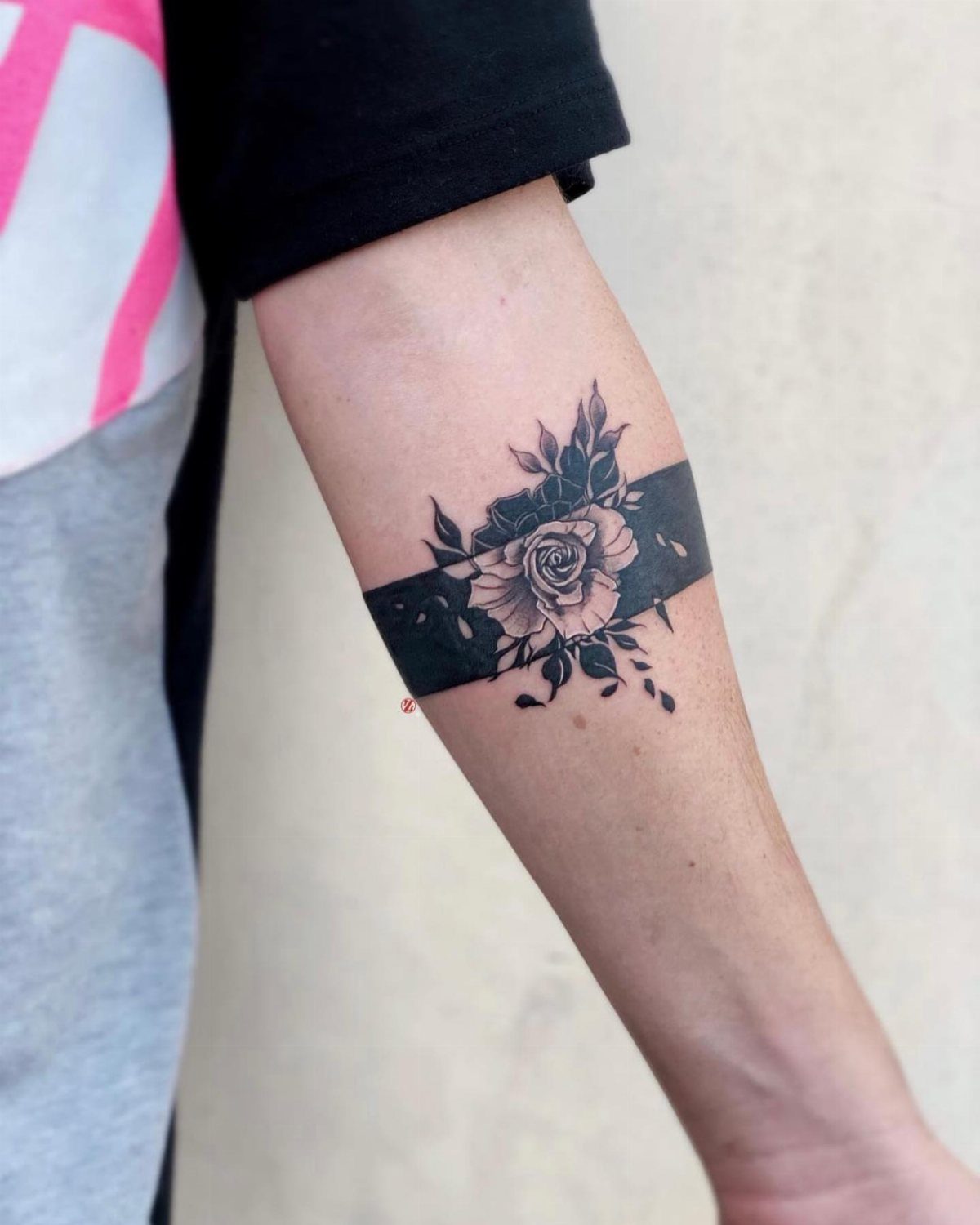7 Rose with Pattern Tattoo Design Ideas for Ink That Stands Out 7 A black and grey rose tattoo with leaves on a person's forearm against a black band.