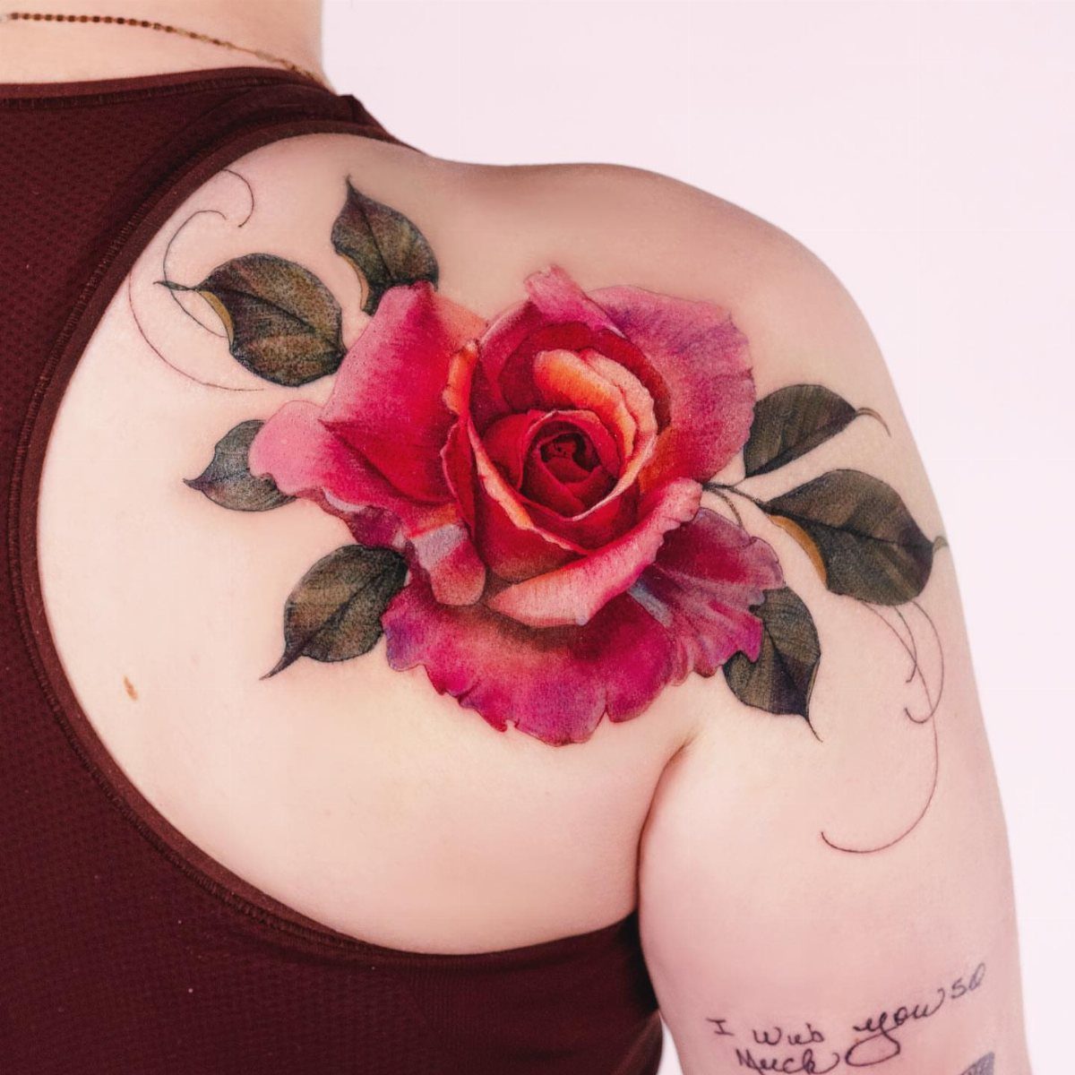 7 Rose with Pattern Tattoo Design Ideas for Ink That Stands Out 6 A colorful rose tattoo with dark leaves and flowing line art on a person's shoulder.