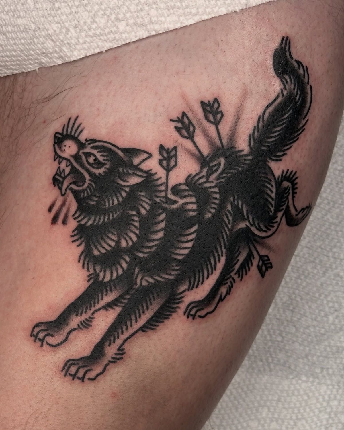Running Wolf Tattoo: 7 Designs That Move 2 A black ink tattoo of a running wolf pierced by several arrows on skin.