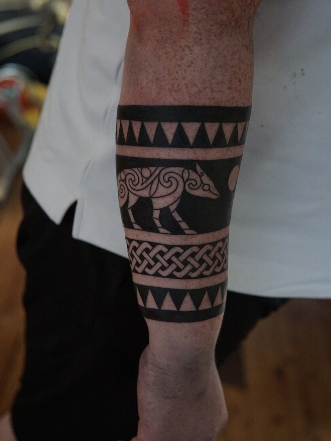 Running Wolf Tattoo: 7 Designs That Move 1 A black ink tribal tattoo of a stylized wolf on a person's forearm.