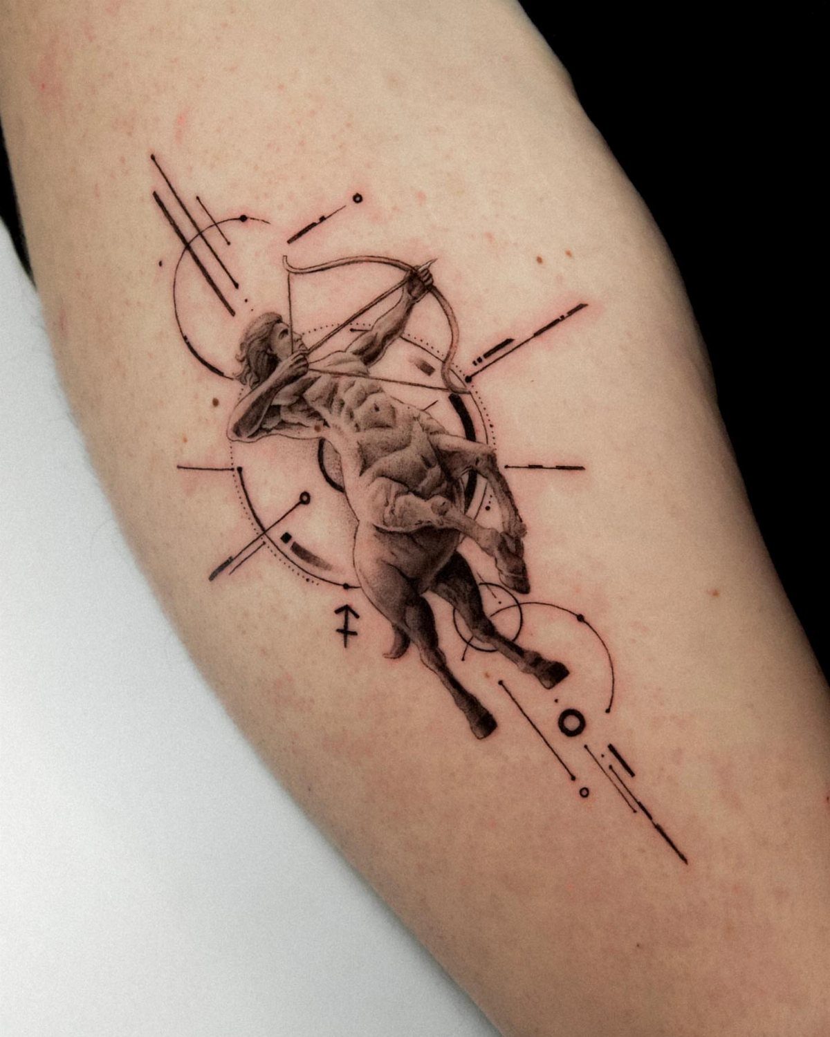 A black and grey centaur archer tattoo with abstract geometric lines on a person's arm.