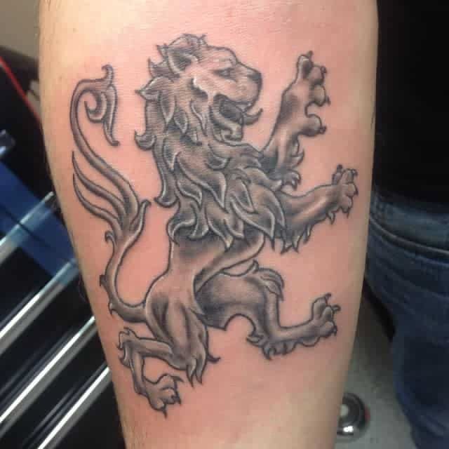 7 Scottish Lion Tattoo Ideas for Your Next Ink 4 A black and grey tattoo of a rampant lion on a person's leg.
