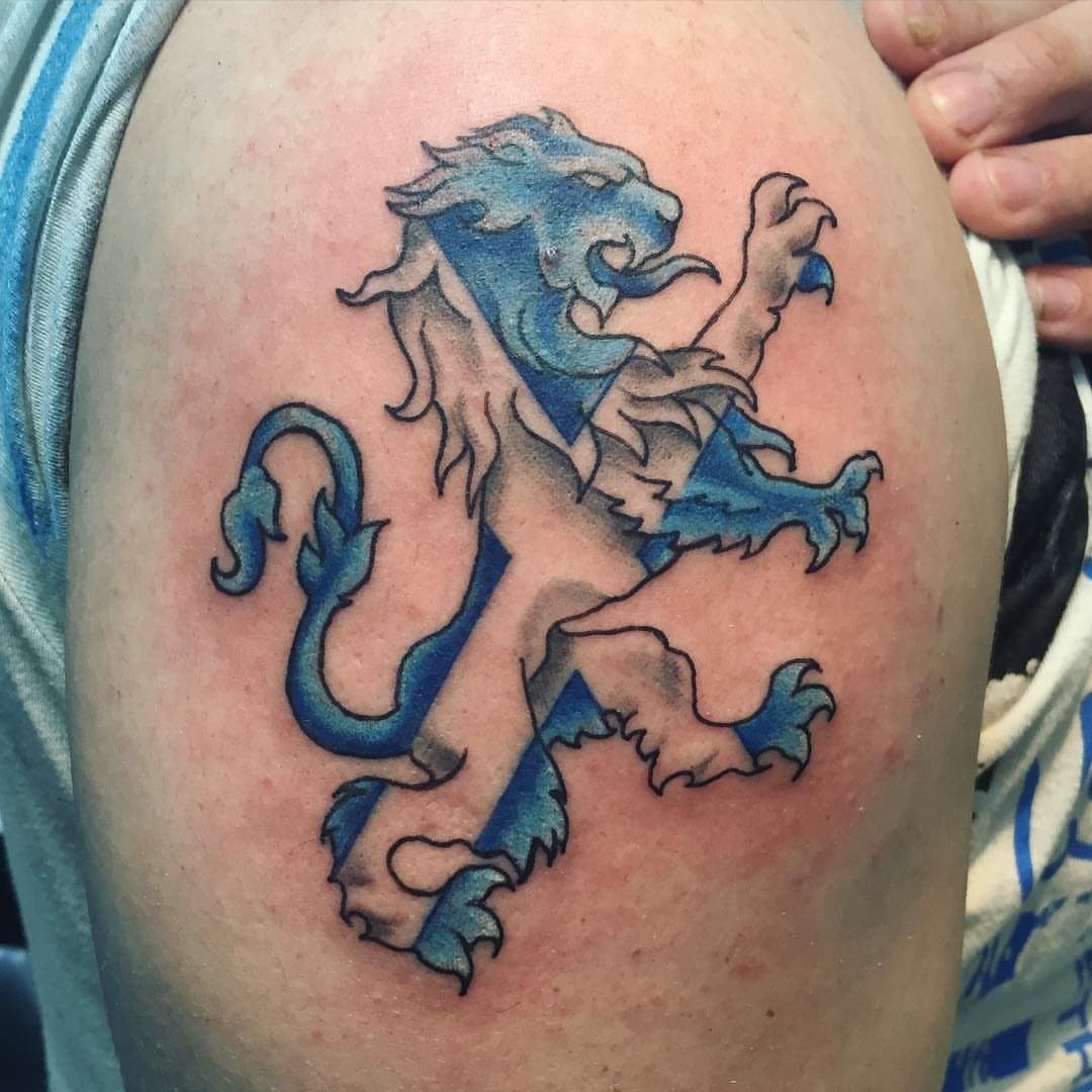 7 Scottish Lion Tattoo Ideas for Your Next Ink 2 A lion rampant tattoo with blue and white Saltire stripes on a person's shoulder.