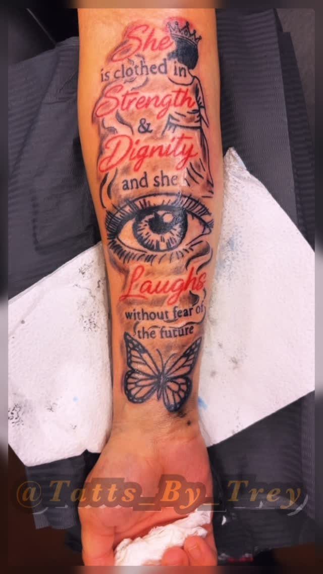 A forearm tattoo featuring a woman's silhouette, an eye, a butterfly, and biblical text in red and black.