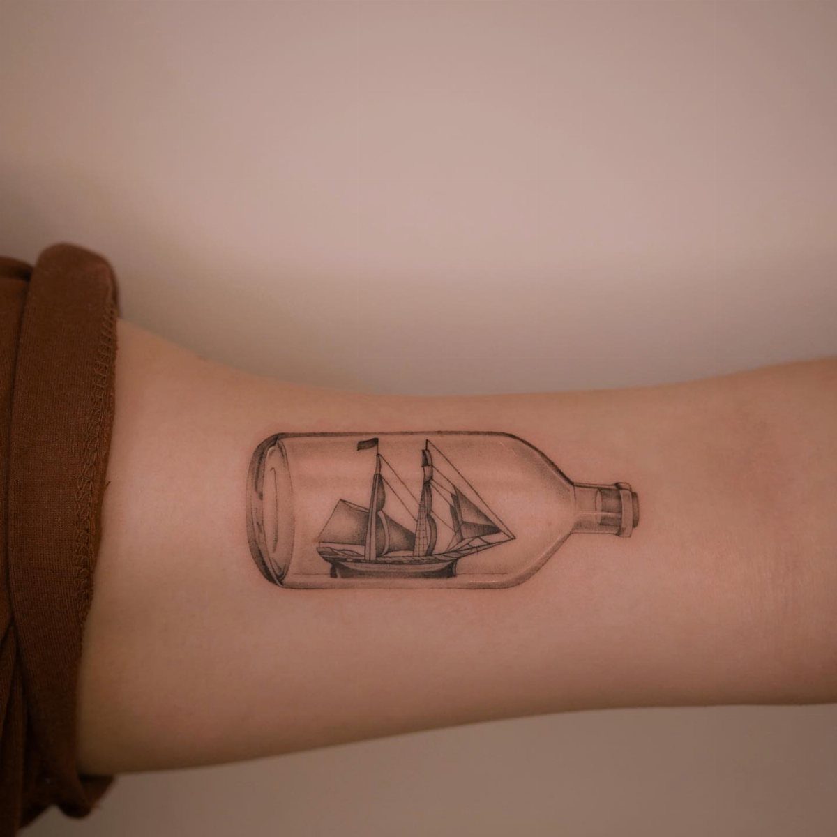 16 Ship Tattoo Ideas in Anchor, Viking, Pirate and Seascape Styles 4 A black and grey tattoo of a sailing ship inside a glass bottle on a wrist.