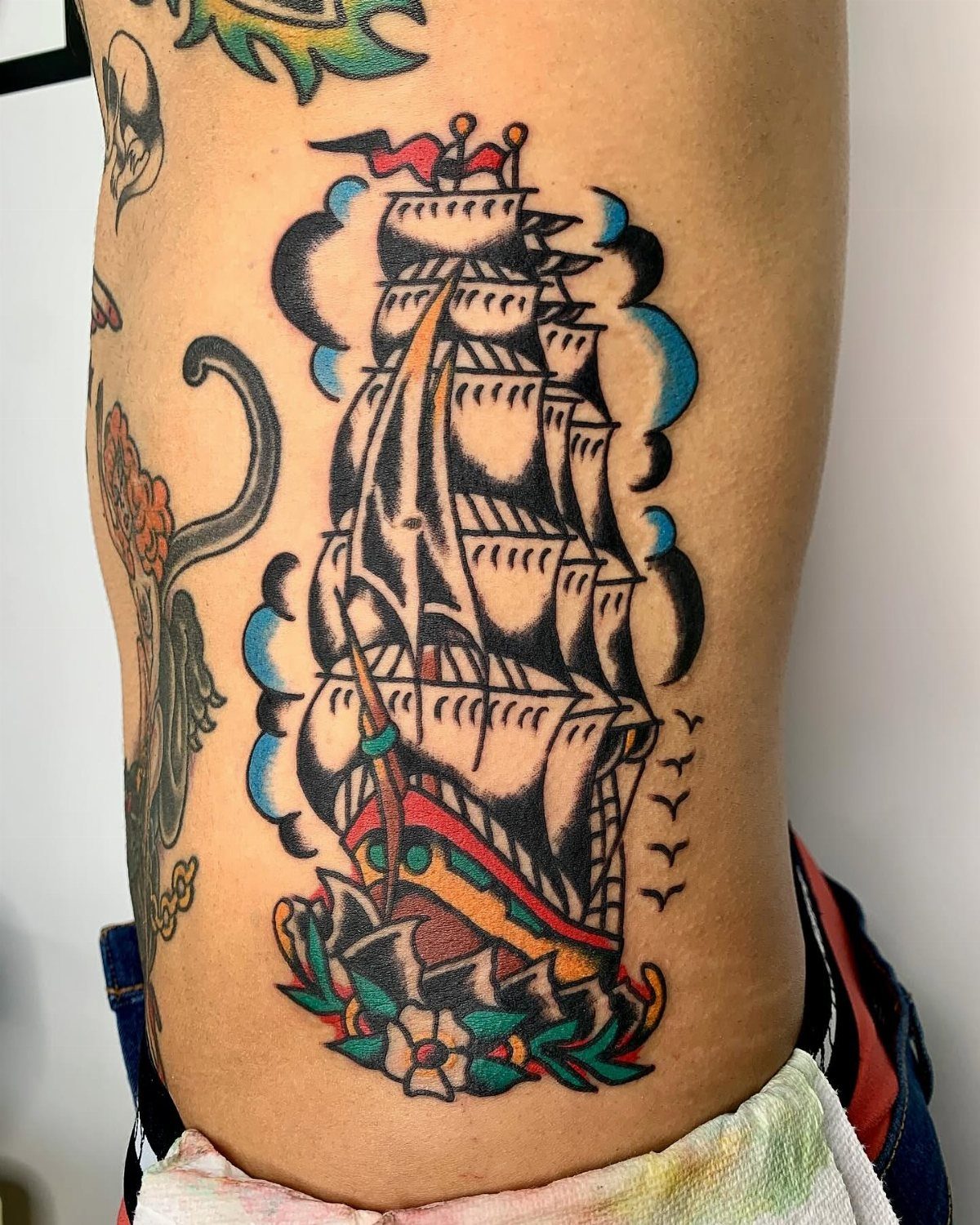 16 Ship Tattoo Ideas in Anchor, Viking, Pirate and Seascape Styles 10 A traditional style clipper ship tattoo with white sails and colorful details on skin.