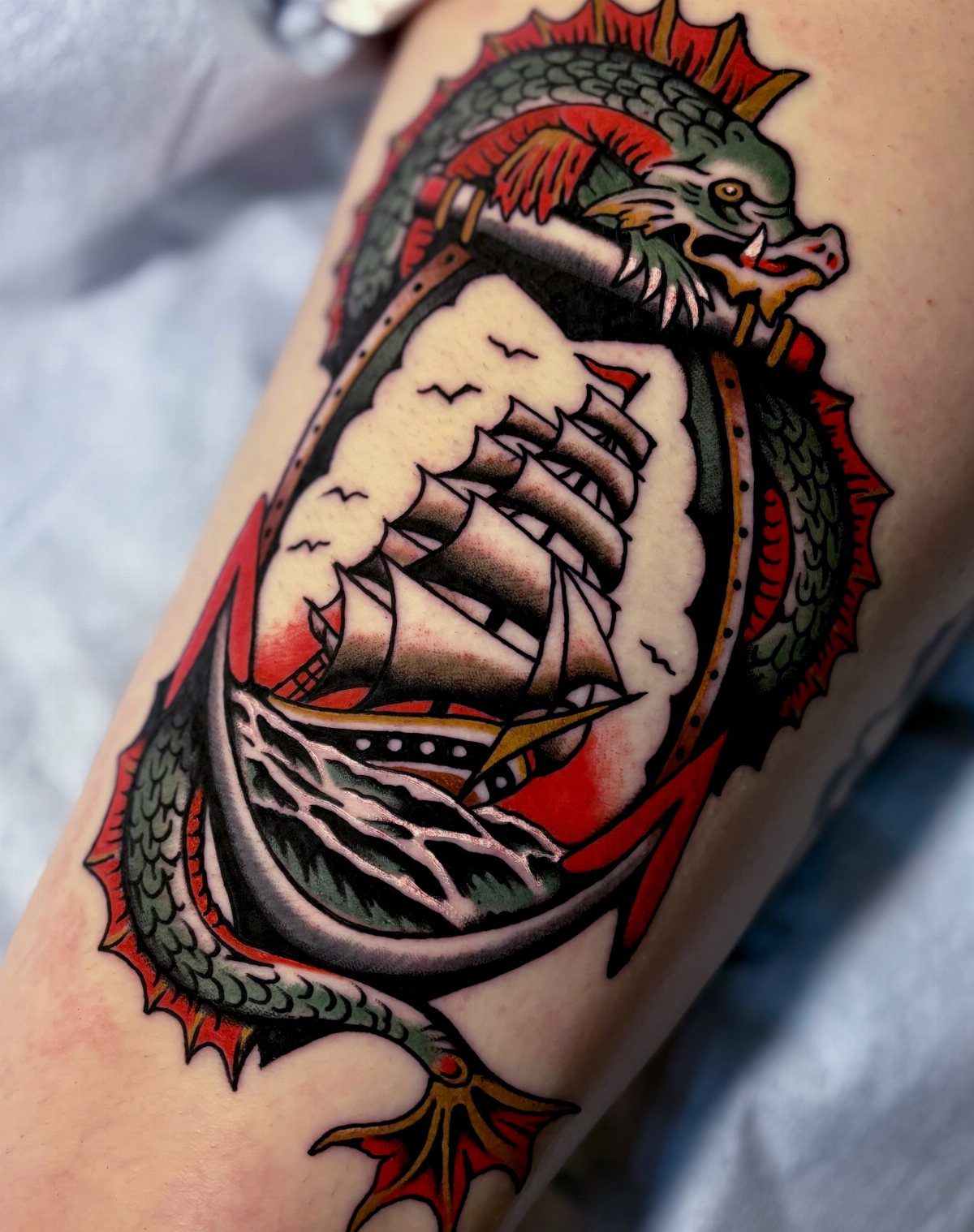 16 Ship Tattoo Ideas in Anchor, Viking, Pirate and Seascape Styles 12 A traditional style tattoo of a sailing ship framed by a green sea dragon on skin.