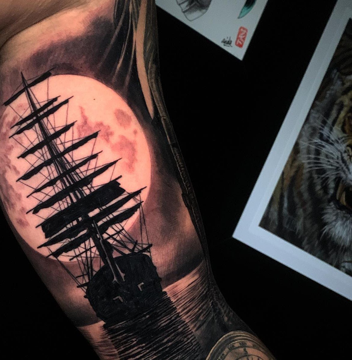 16 Ship Tattoo Ideas in Anchor, Viking, Pirate and Seascape Styles 9 A detailed black and grey tattoo of a sailing ship silhouetted against a large moon.
