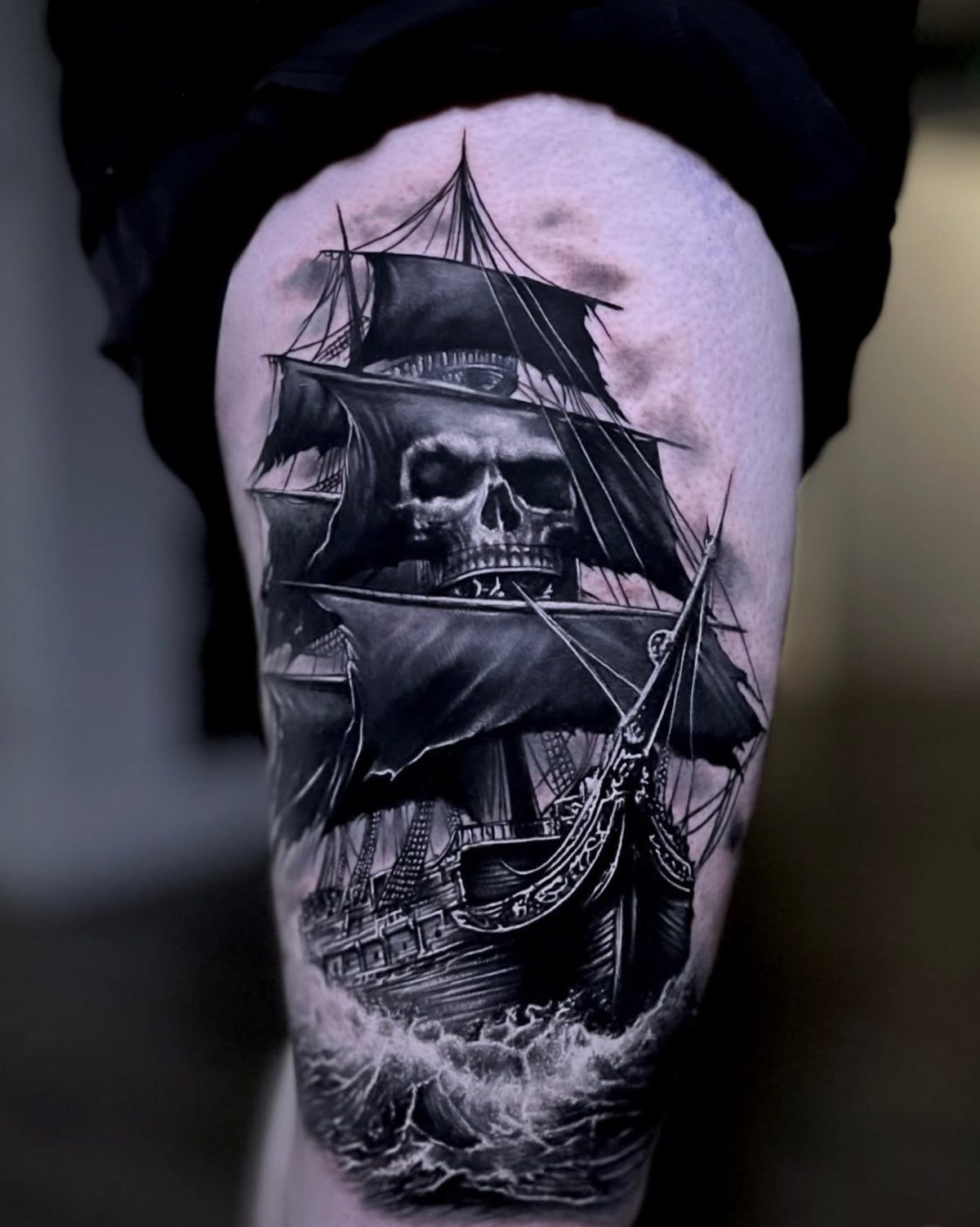 16 Ship Tattoo Ideas in Anchor, Viking, Pirate and Seascape Styles 11 A large black and grey tattoo of a sailing ship with a skull in the sails.