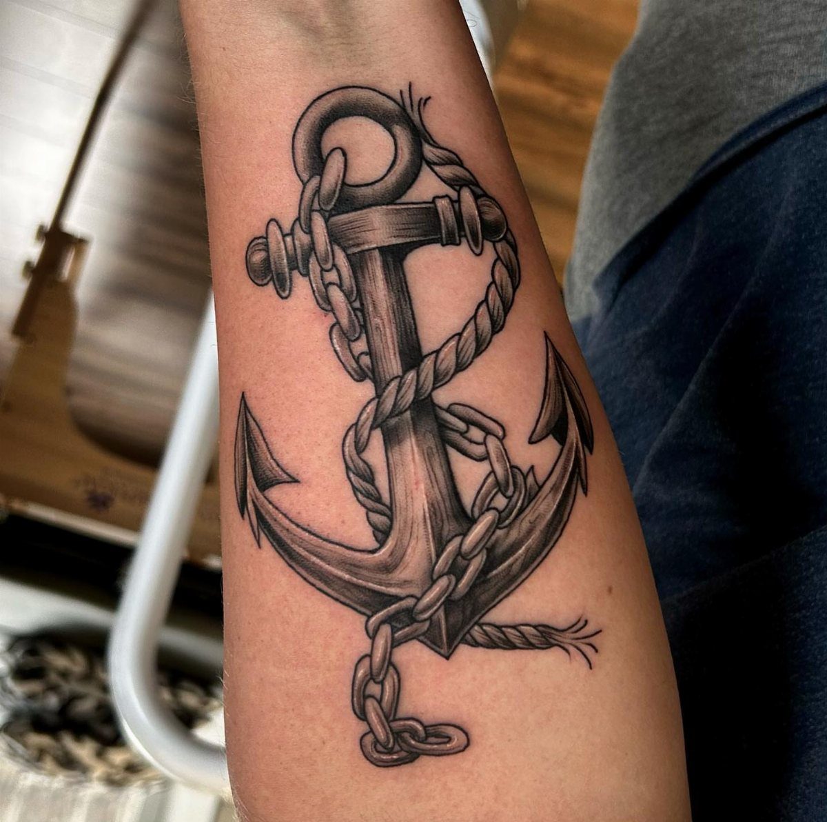16 Ship Tattoo Ideas in Anchor, Viking, Pirate and Seascape Styles 1 A black and gray anchor tattoo with rope wrapped around it on a person's forearm.