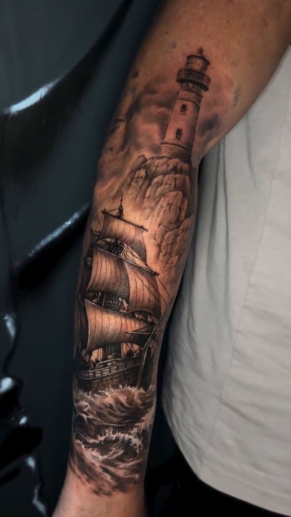 16 Ship Tattoo Ideas in Anchor, Viking, Pirate and Seascape Styles 14 A detailed black and grey forearm tattoo of a sailing ship and a lighthouse.