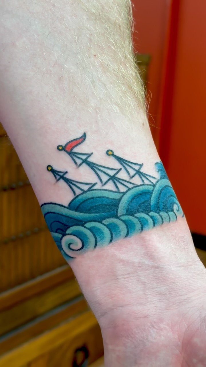 16 Ship Tattoo Ideas in Anchor, Viking, Pirate and Seascape Styles 15 A colorful tattoo of a sailing ship on blue waves wrapped around a person's wrist.