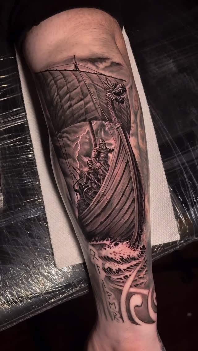 16 Ship Tattoo Ideas in Anchor, Viking, Pirate and Seascape Styles 2 A detailed black and grey Viking longship tattoo on a person's forearm amidst stormy waves.