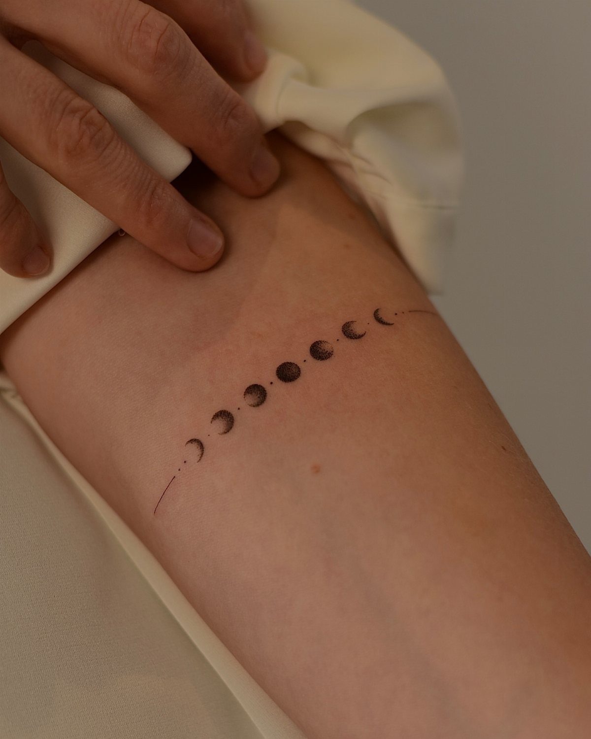 7 Simple Moon Phase Tattoo Designs for Every Style 2 A horizontal line of black ink moon phase tattoos on a person's forearm.