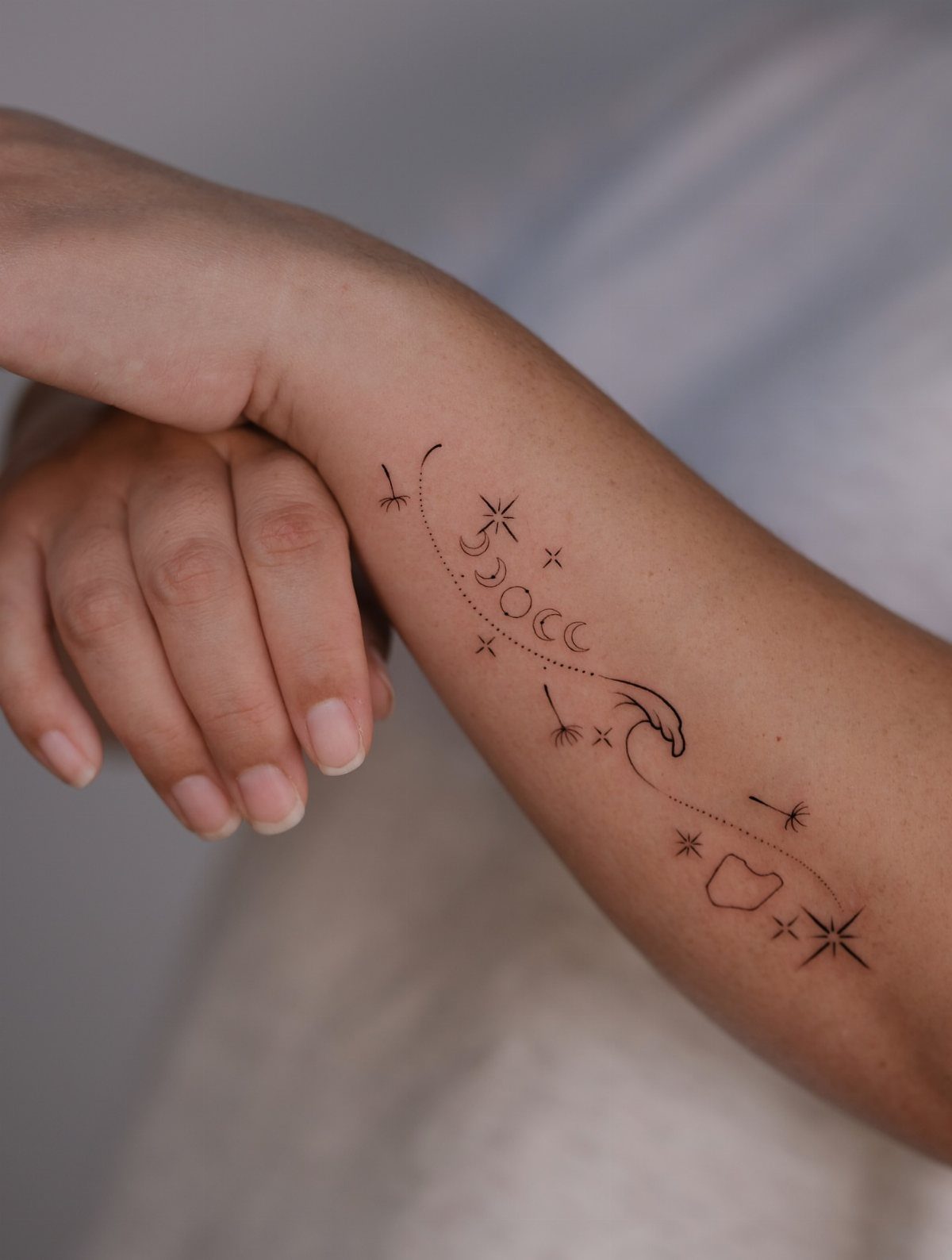 7 Simple Moon Phase Tattoo Designs for Every Style 3 A fine line black ink tattoo of moon phases and stars on a person's forearm.