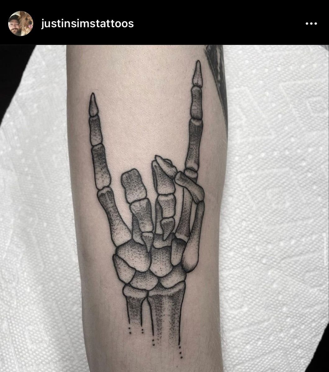 7 Skeleton Hand Tattoo Ideas for Your Next Ink 4 A dotwork tattoo of a skeleton hand making a rock and roll gesture on an arm.