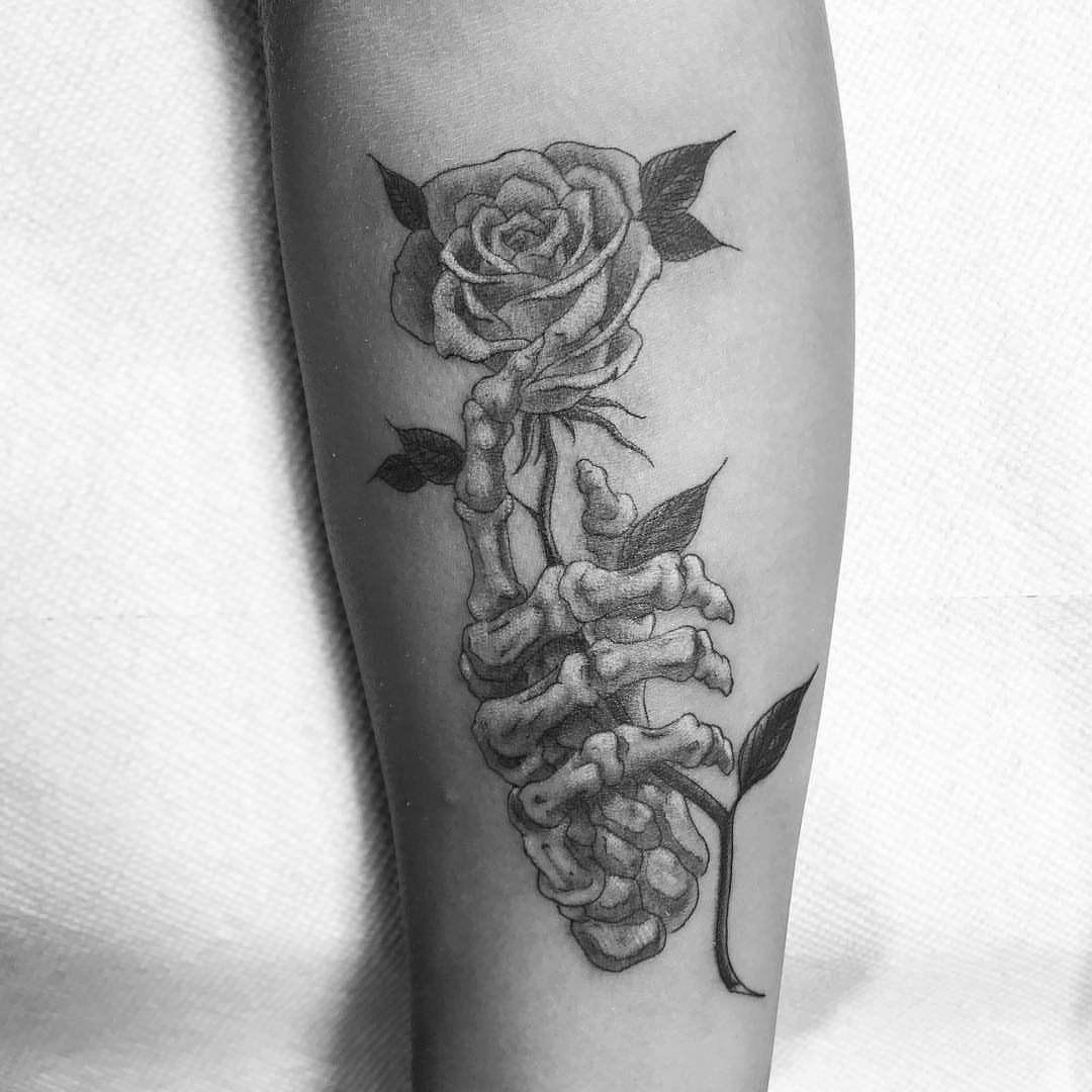 7 Skeleton Hand Tattoo Ideas for Your Next Ink 3 A black and grey tattoo of a skeleton hand holding a rose on an arm.