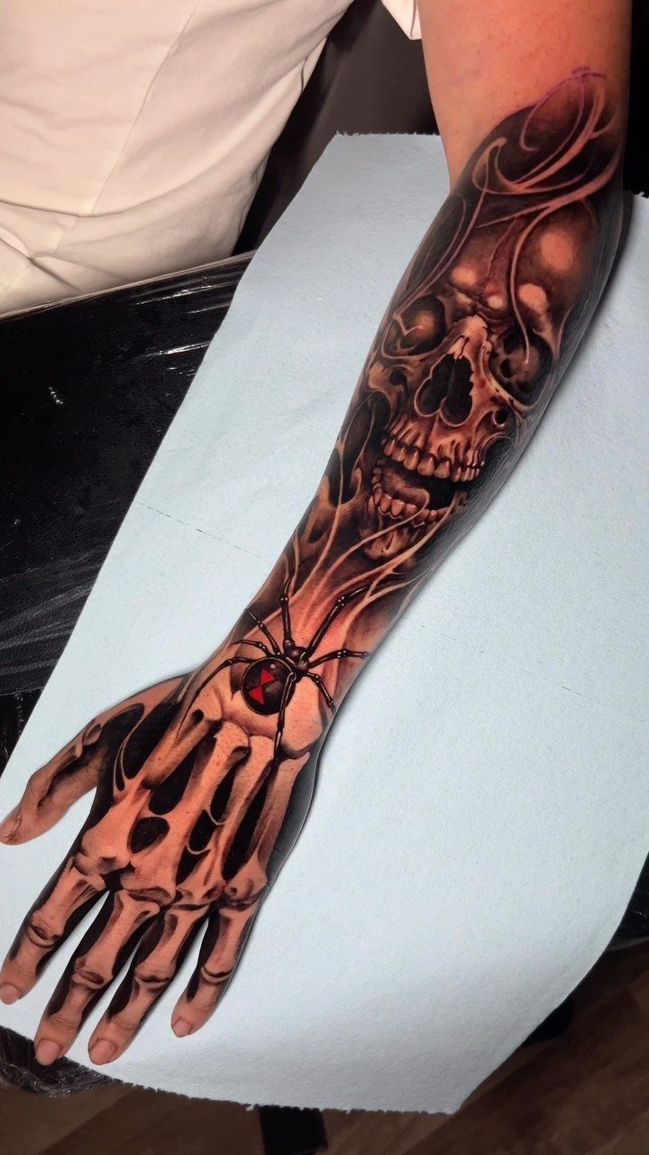 7 Skeleton Hand Tattoo Ideas for Your Next Ink 7 A detailed black and grey tattoo of a skull on a forearm and a skeleton hand.
