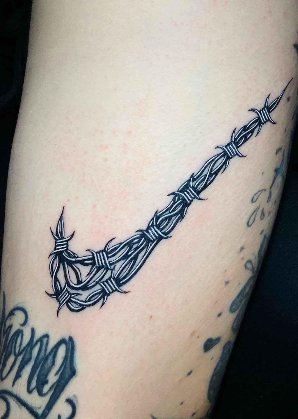 9 Sneaker Tattoo Ideas for Streetwear and Sport Ink 7 A black ink tattoo of a Nike swoosh made from barbed wire on skin.