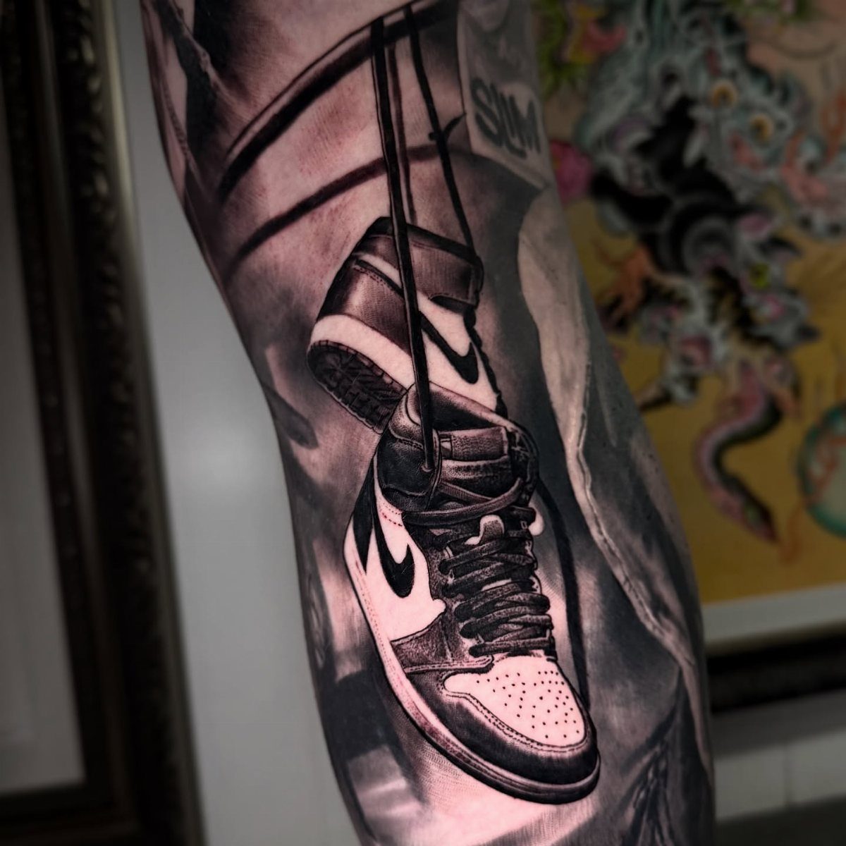 9 Sneaker Tattoo Ideas for Streetwear and Sport Ink 1 A black and grey realism tattoo of two high-top sneakers hanging by their laces on a leg.