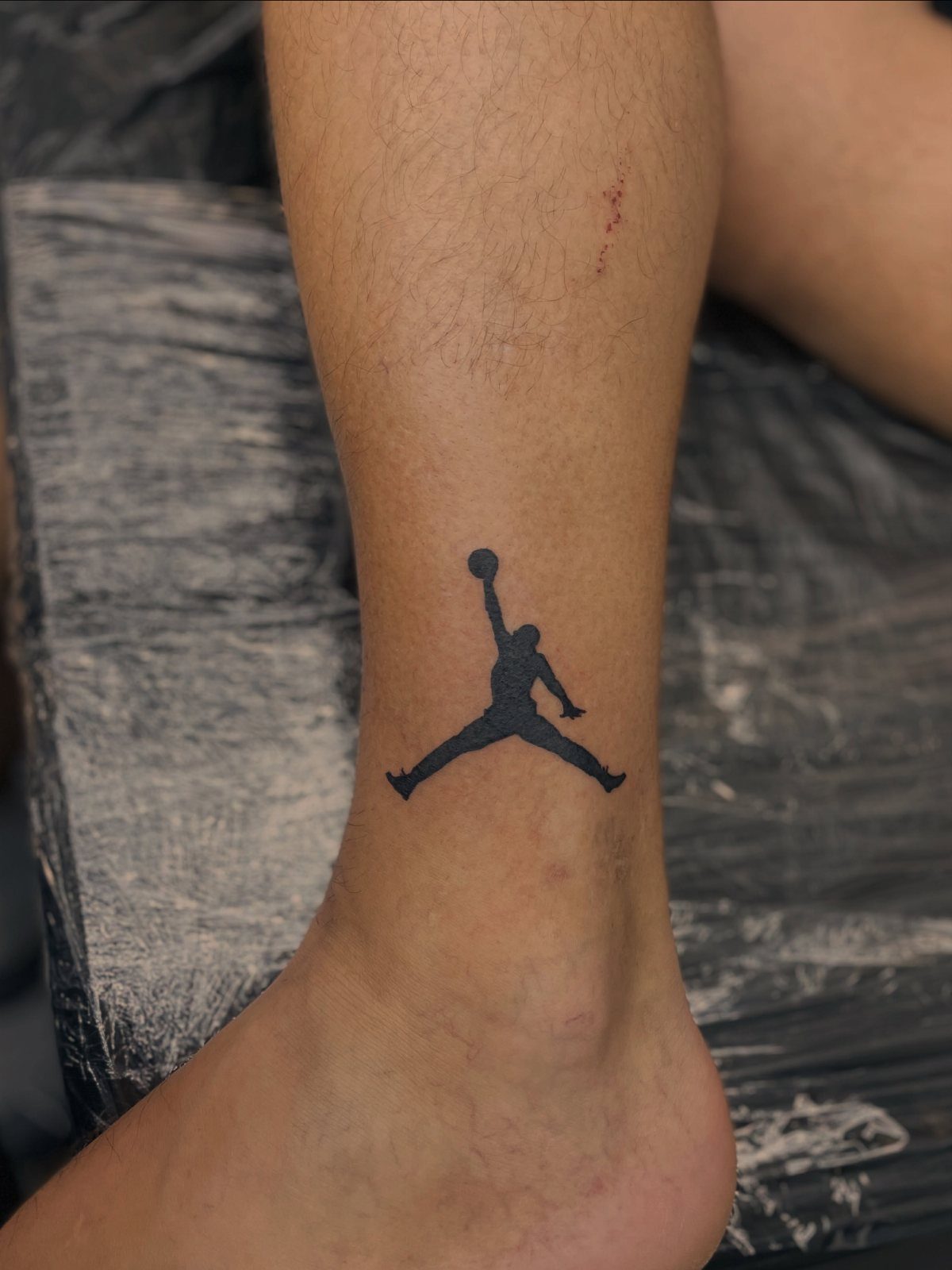 9 Sneaker Tattoo Ideas for Streetwear and Sport Ink 8 A black Jumpman logo tattoo on a person's lower leg above the ankle.