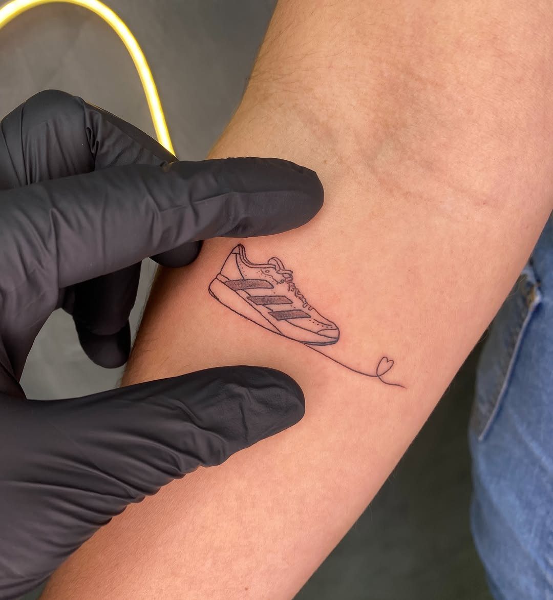 9 Sneaker Tattoo Ideas for Streetwear and Sport Ink 4 A minimalist black ink tattoo of a striped sneaker with a small heart at the end of a line.