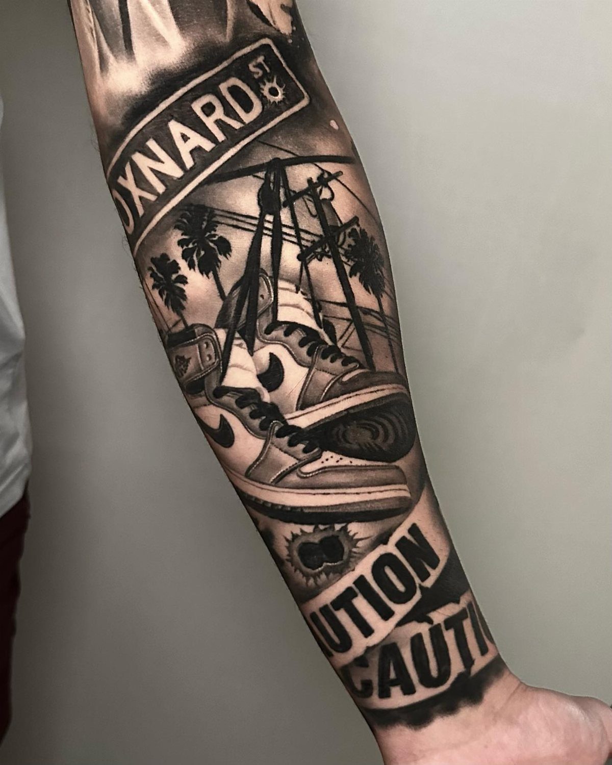 9 Sneaker Tattoo Ideas for Streetwear and Sport Ink 9 A black and grey forearm tattoo featuring high-top sneakers, palm trees, and street signs.