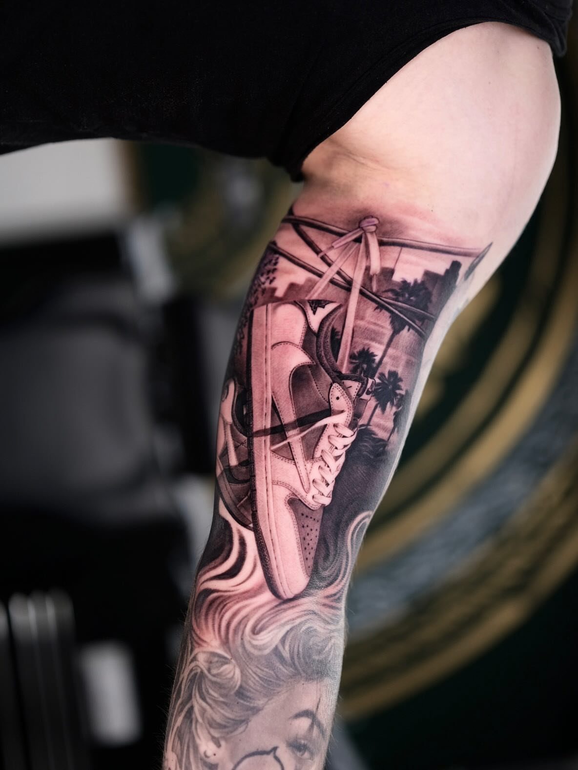9 Sneaker Tattoo Ideas for Streetwear and Sport Ink 3 A detailed black and grey tattoo of a high-top sneaker and palm trees on a leg.