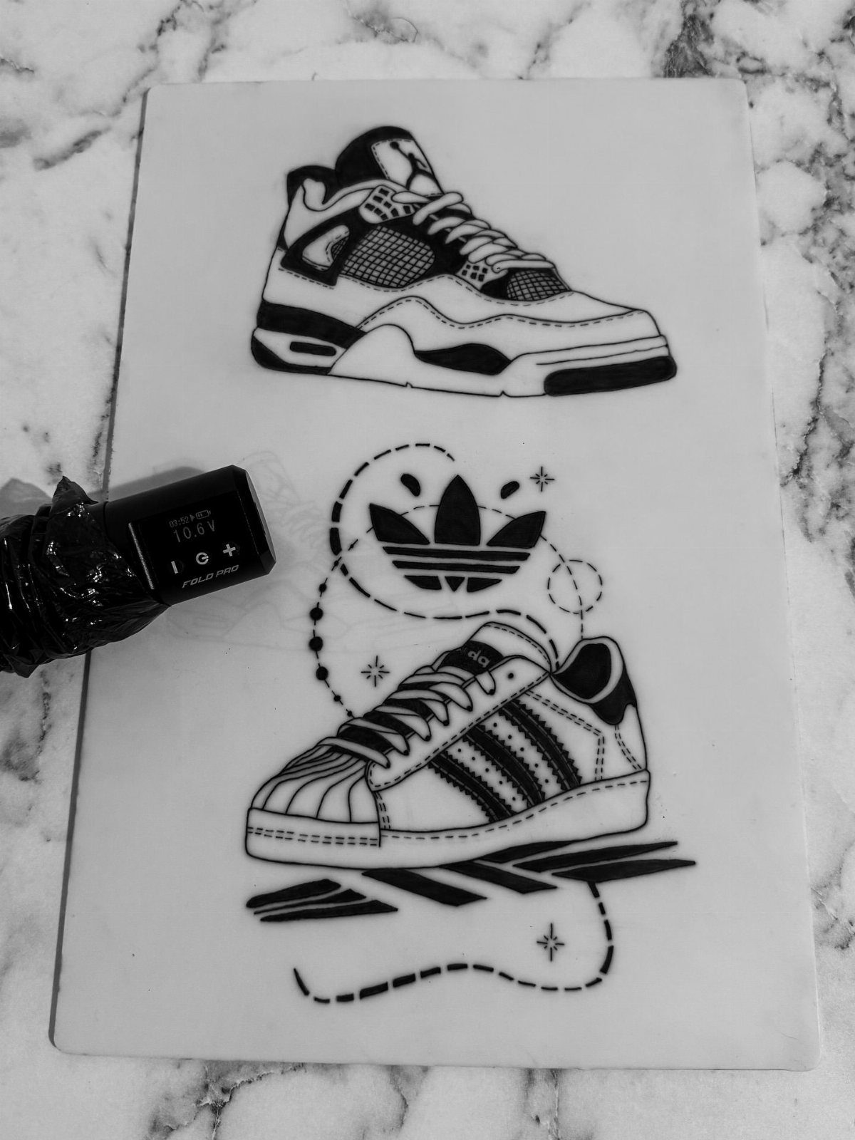 9 Sneaker Tattoo Ideas for Streetwear and Sport Ink 5 Black ink drawings of two different sneakers on a white marble surface.