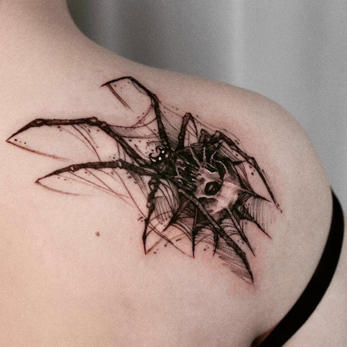 12 Spider Tattoo Ideas That Balance Creepy and Beautiful 2 A black ink abstract spider tattoo with sharp geometric lines on a person's shoulder.