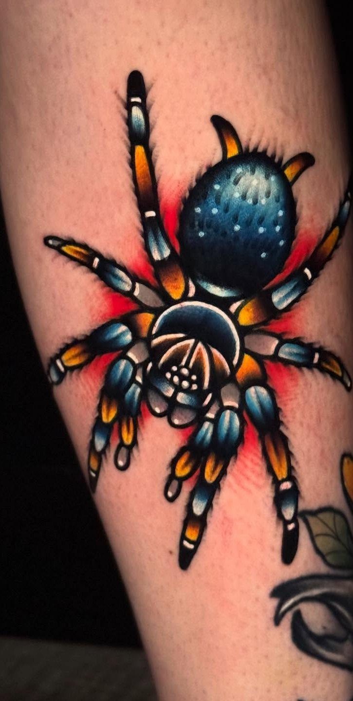 12 Spider Tattoo Ideas That Balance Creepy and Beautiful 12 A vibrant spider tattoo with blue, orange, and red ink on human skin.